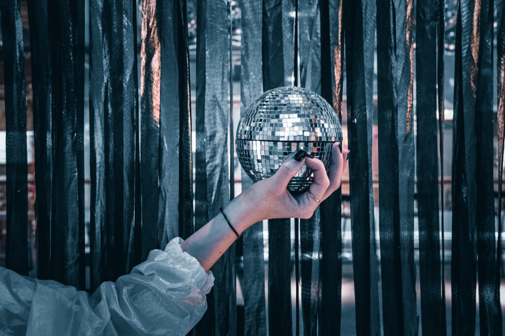 Eine Hand hält eine Discokugel vor einem Vorhang aus dunklen Bändern.