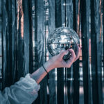 Eine Hand hält eine Discokugel vor einem Vorhang aus dunklen Bändern.