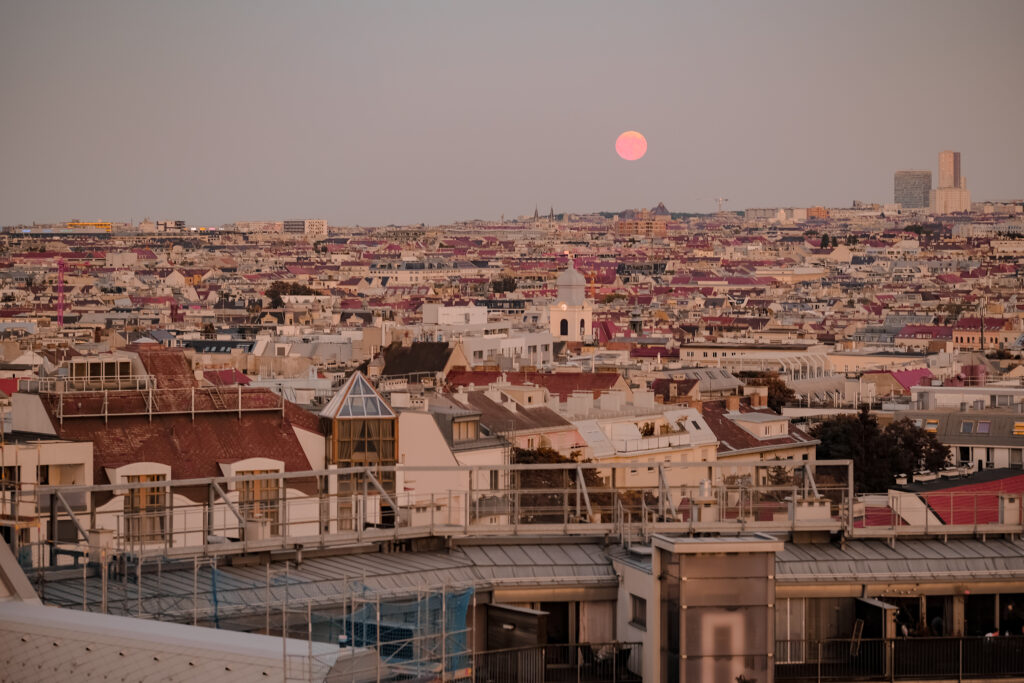 Blick über die Dächer von Wien in der Dämmerung, ein rosafarbener Vollmond steht über der Stadt.