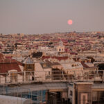 Blick über die Dächer von Wien in der Dämmerung, ein rosafarbener Vollmond steht über der Stadt.