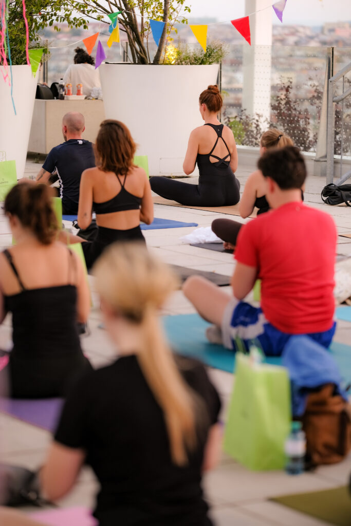 Yogagruppe sitzt bei Abendlicht auf Matten auf einer Dachterrasse, im Hintergrund die Stadt.