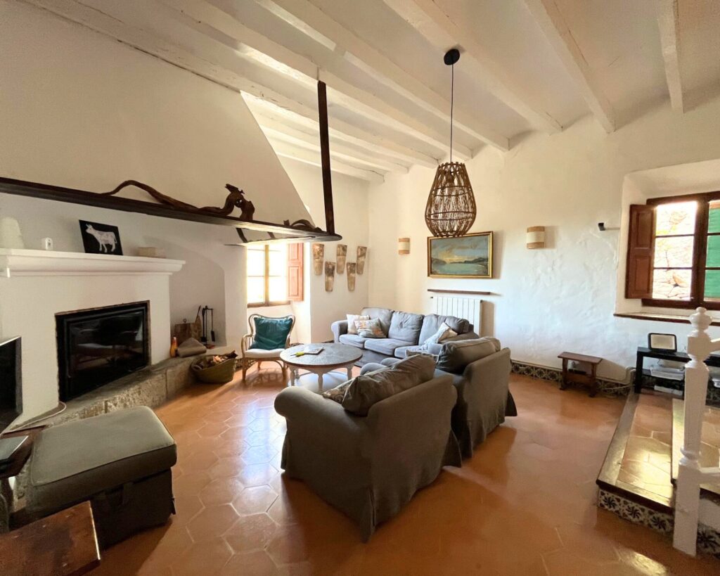 Wohnzimmer mit offenem Kamin, grauen Sofas und Terrakottaboden.