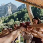 Gruppe stößt unter einer Pergola mit Gläsern an, im Hintergrund die Berge.
