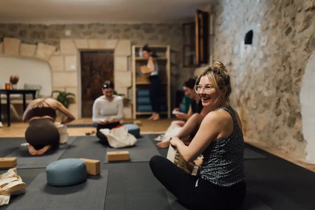 Yogaraum in einem Gewölbe aus Naturstein, eine Frau mit Brille lacht in die Kamera.