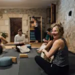 Yogaraum in einem Gewölbe aus Naturstein, eine Frau mit Brille lacht in die Kamera.