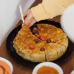Tortilla in einer Pfanne, daneben Tomaten; eine Hand setzt ein Messer an.