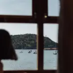 Blick aus dem Fenster der historischen Tram auf Port de Sóller mit dem Leuchtturm, links die Silhouette einer Mitfahrerin.