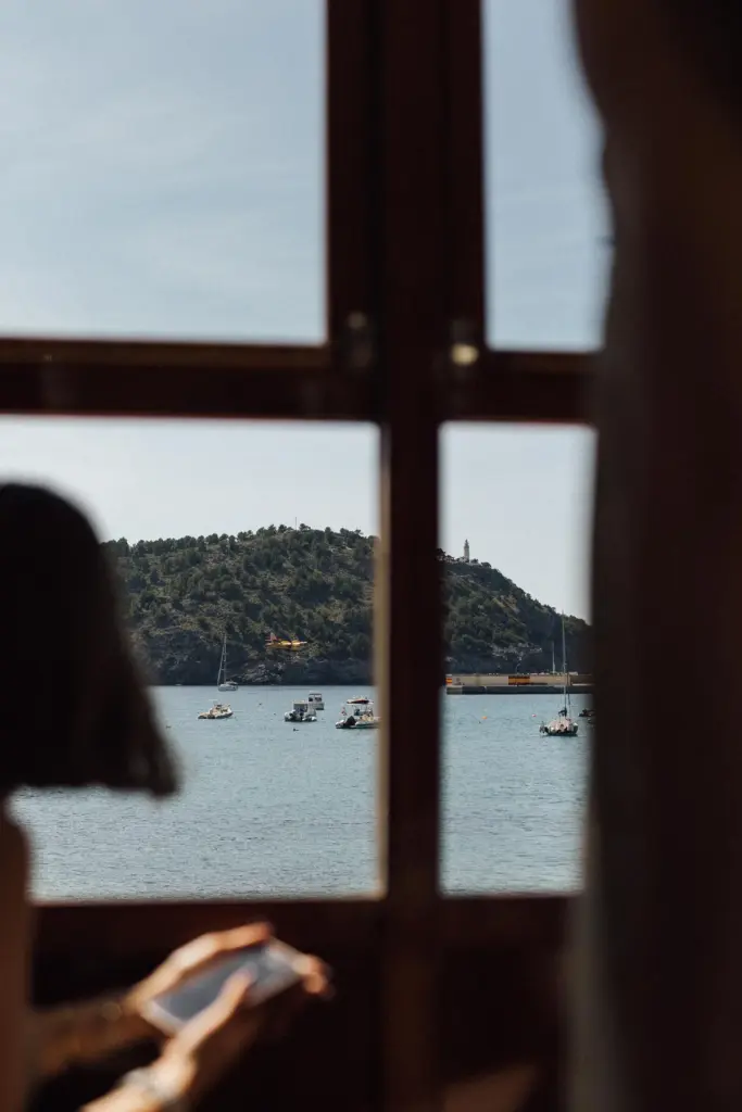 Blick aus dem Fenster der historischen Tram auf Port de Sóller mit dem Leuchtturm, links die Silhouette einer Mitfahrerin.