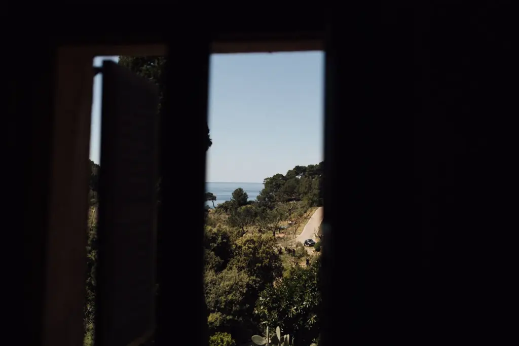 Blick durch ein Fenster aus einem dunklen Raum hinaus auf das Meer.