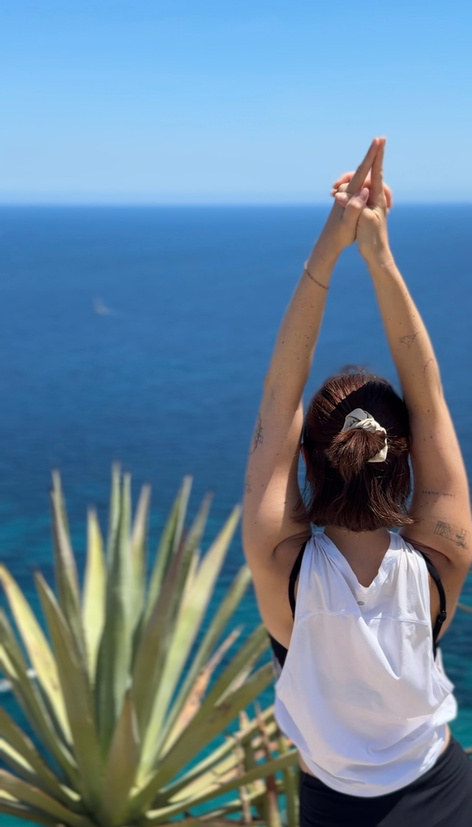 Yoga am Meer: Haende ueber dem Kopf zusammengefuehrt, im Hintergrund das Wasser